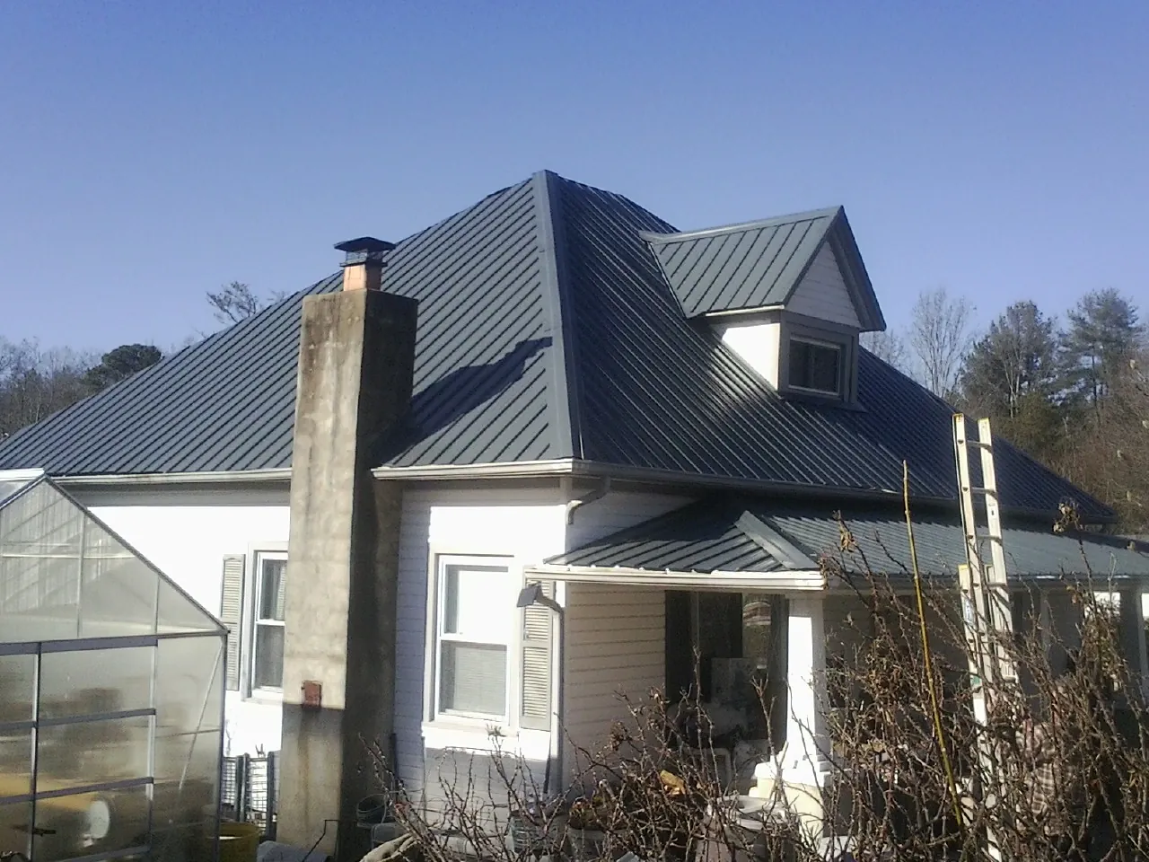 Dark blue standing seam metal roof on a white farmhouse with dormer — Slate & Tile Roof Repair by Roofing Brothers in Masury