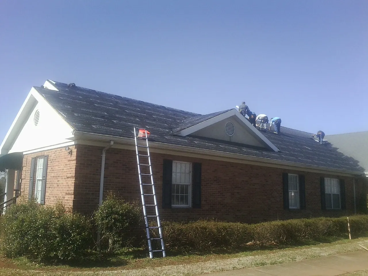 Crew tearing shingles off a brick ranch roof with a ladder set — Metal Roof Repair work by our crew in Masury