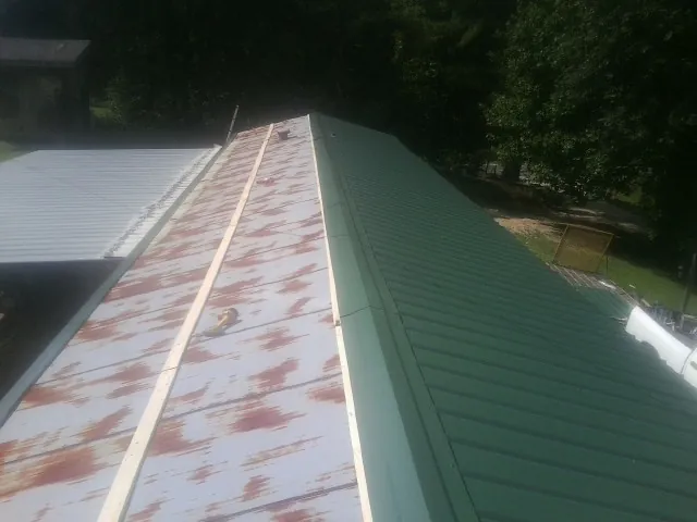 Old rusted panels beside newly installed green metal roofing — Wind Damage Roof Repair by Roofing Brothers in Masury
