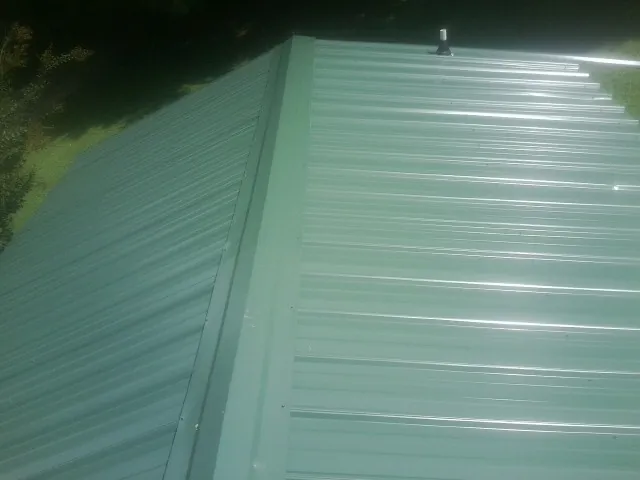 New green metal panels meeting at the ridge of a roof — Flat Roof Repair work by our crew in Masury