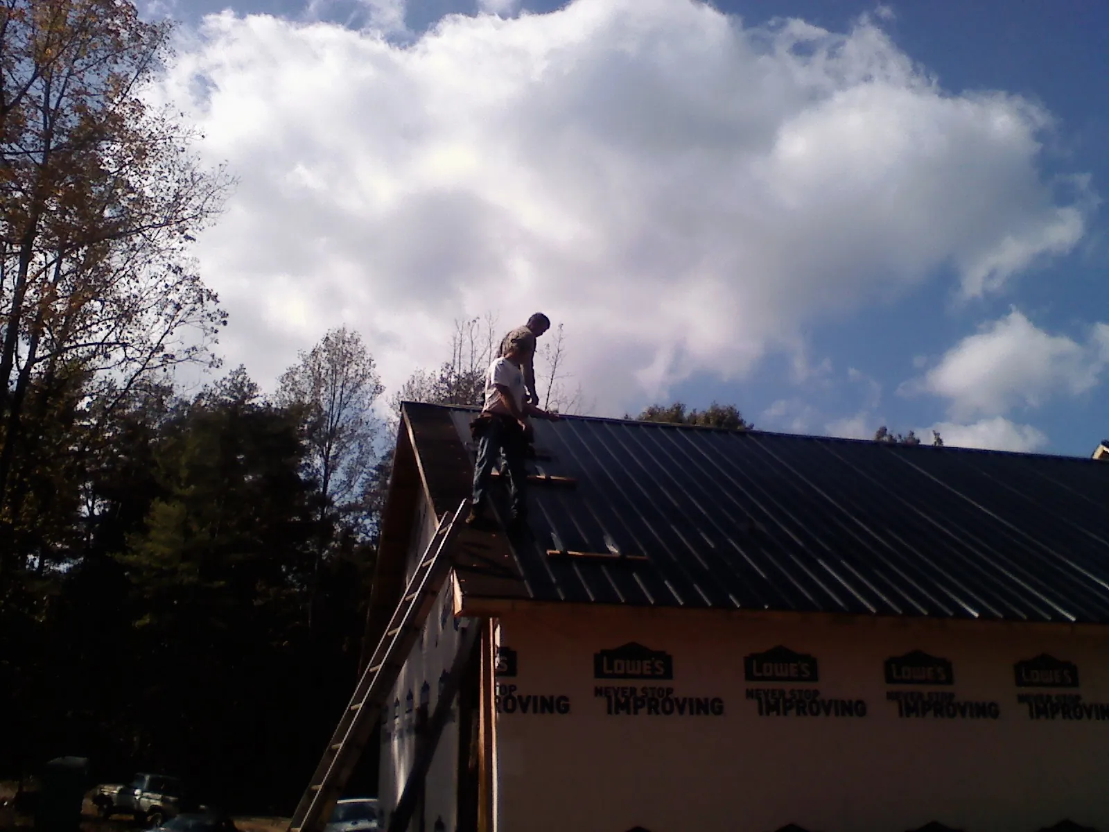 Roofer fastening dark metal panels high against a cloudy sky, from a Roof Inspection job in Masury